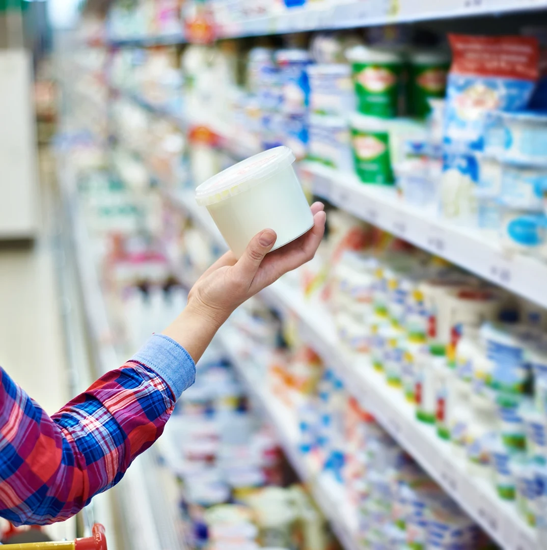 Person choosing yogurt in grocery store.