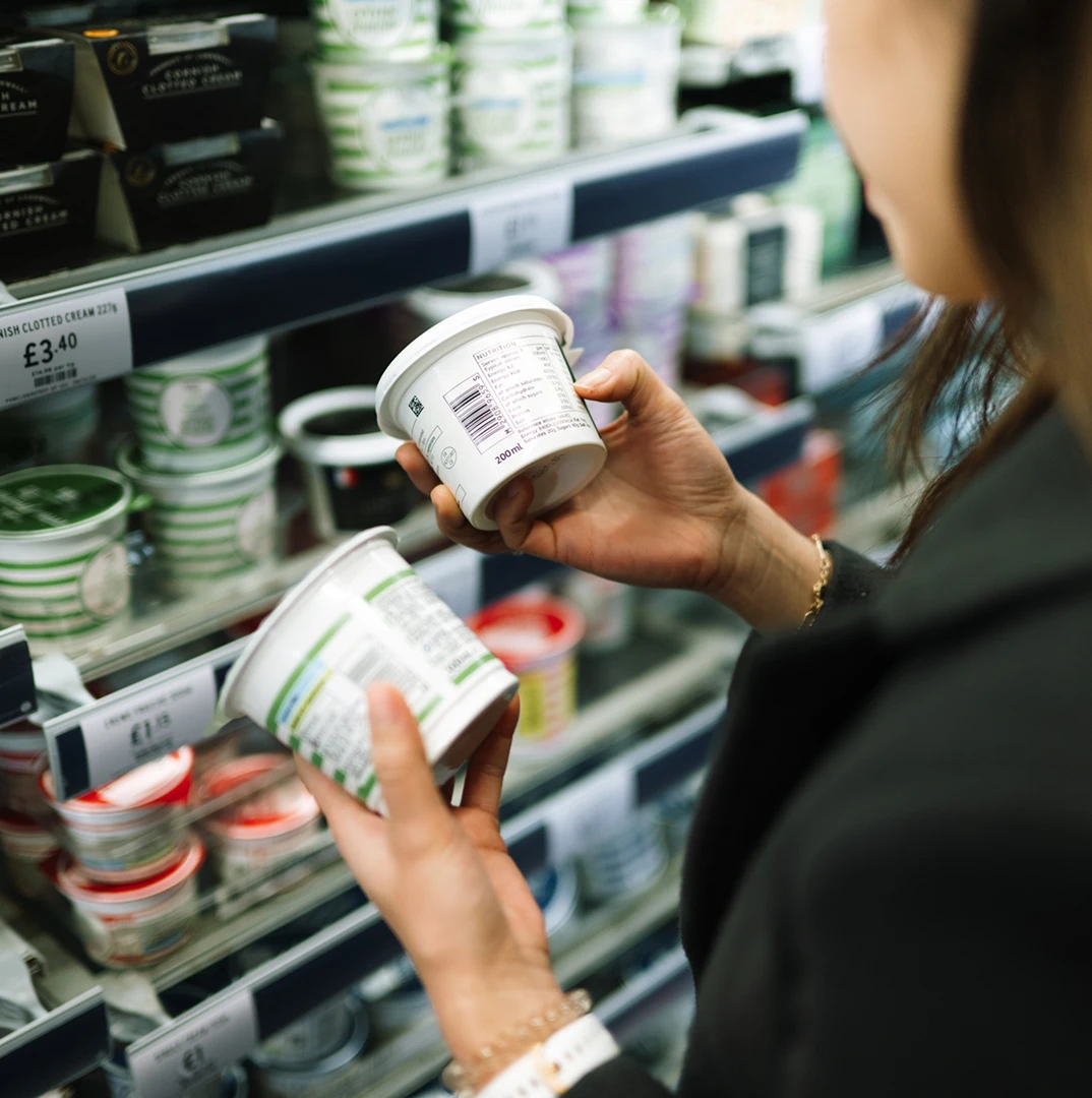 Person comparing yogurt containers in store.